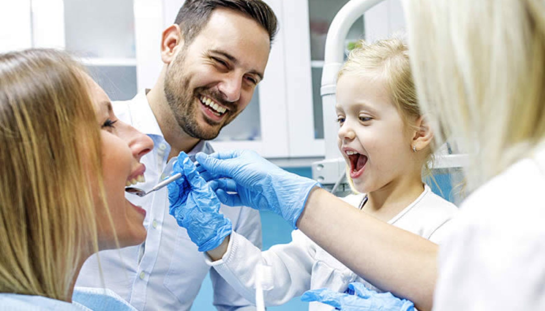 Bro eller Implantat: Hva Er Det Beste Valget for Et Manglende Tannrom? 14 Tannlege undersøker mors tenner mens far og lite barn ler sammen under vennlig tannlegebesøk i moderne klinikkrom utstyr