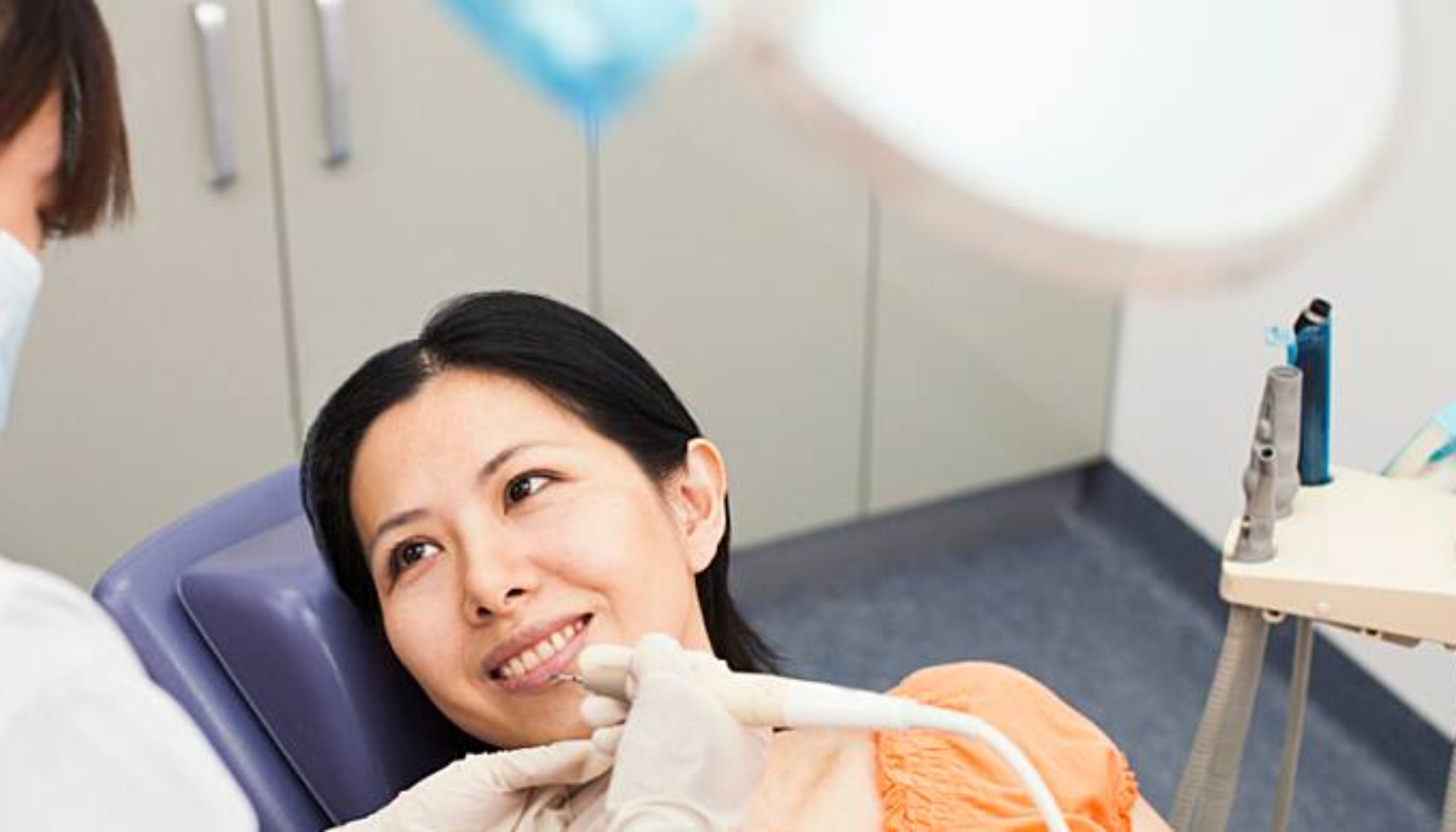 Trekke tann pris – Dette må du vite før behandling 11 Kvinne ligger i tannlegestol og smiler mens tannlegen utfører undersøkelse. Klinikkmiljø med moderne utstyr og rolige omgivelser.