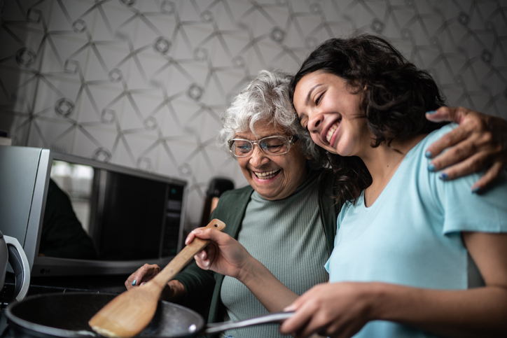 Gray haired grandma and granddaughter cooking on the stove. 