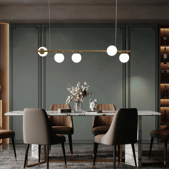 Linear brass pendant light with globe bulbs suspended above a modern dining table.