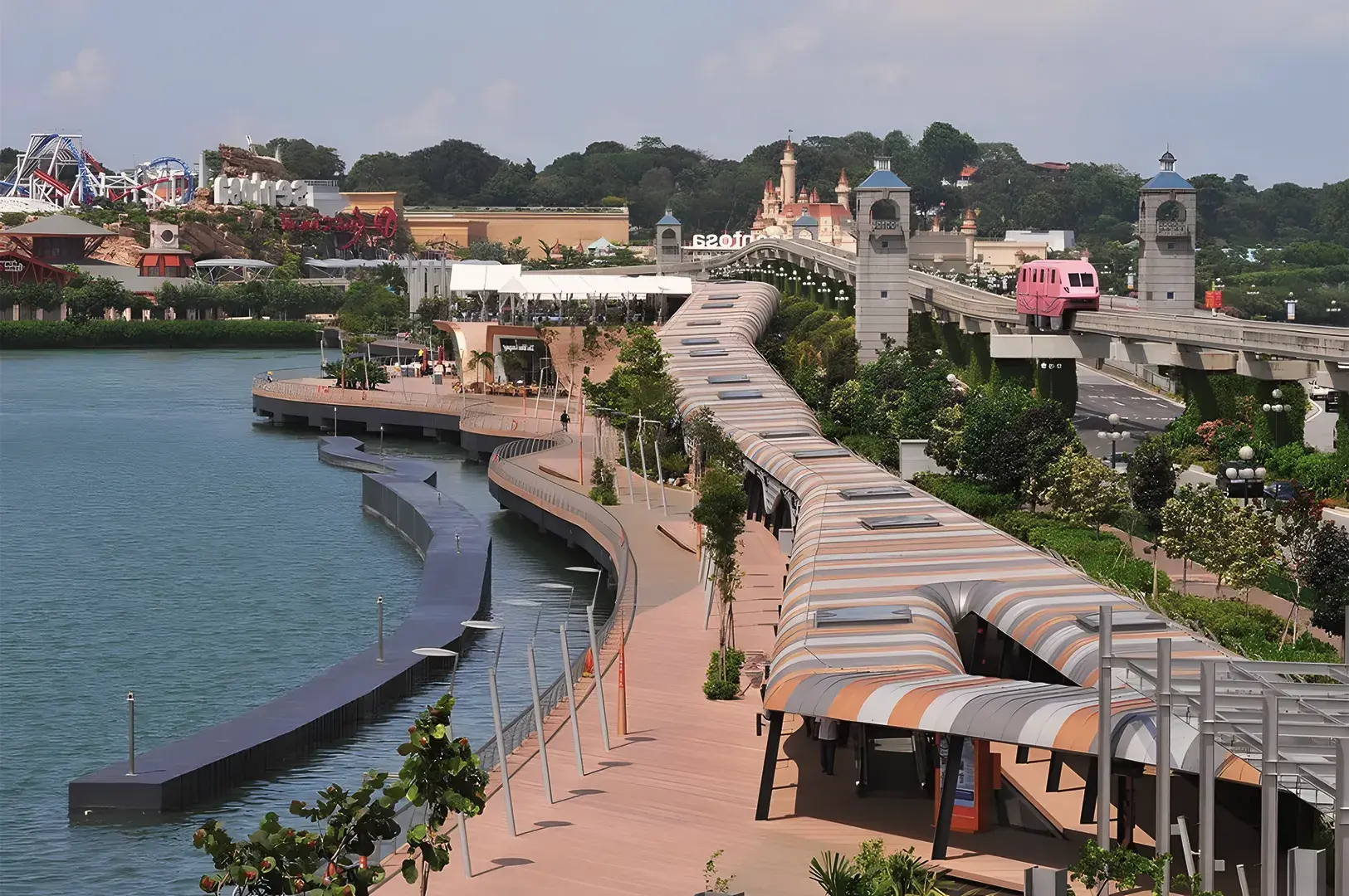 Sentosa Boardwalk and monorail leading to Universal Studios Singapore with waterfront views, lush greenery, and amusement park attractions in the background.