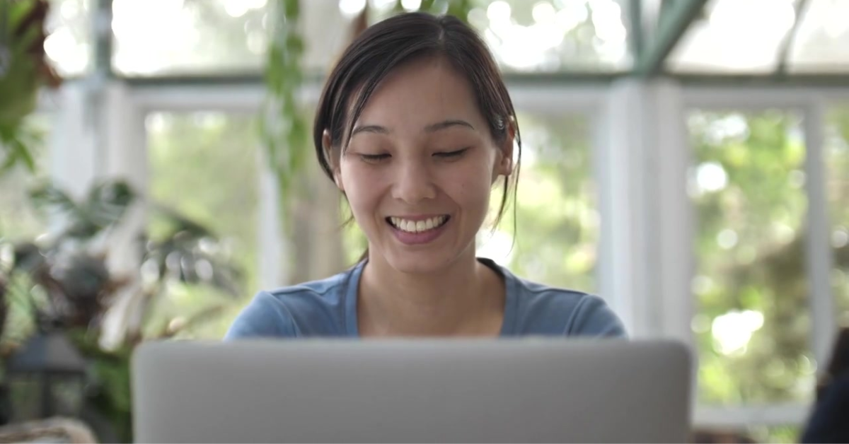 A smiling woman working on her laptop indoors, reviewing her self employed tax return form for submission.