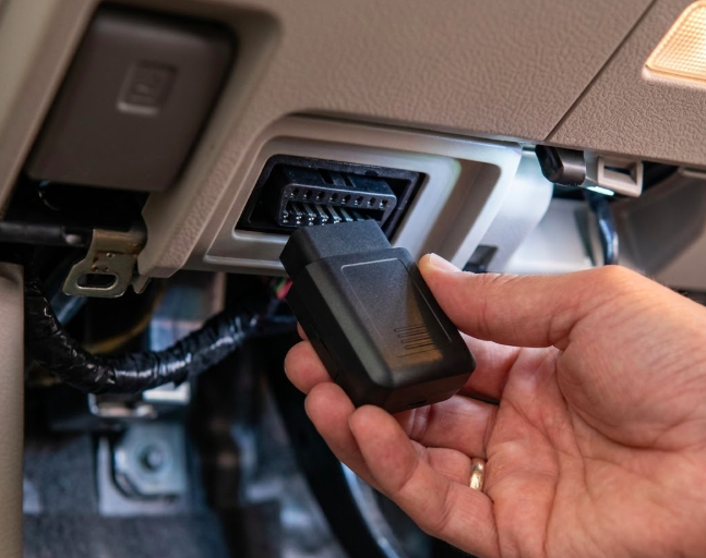 OBD II GPS tracker plugged into car diagnostic port under the dashboard