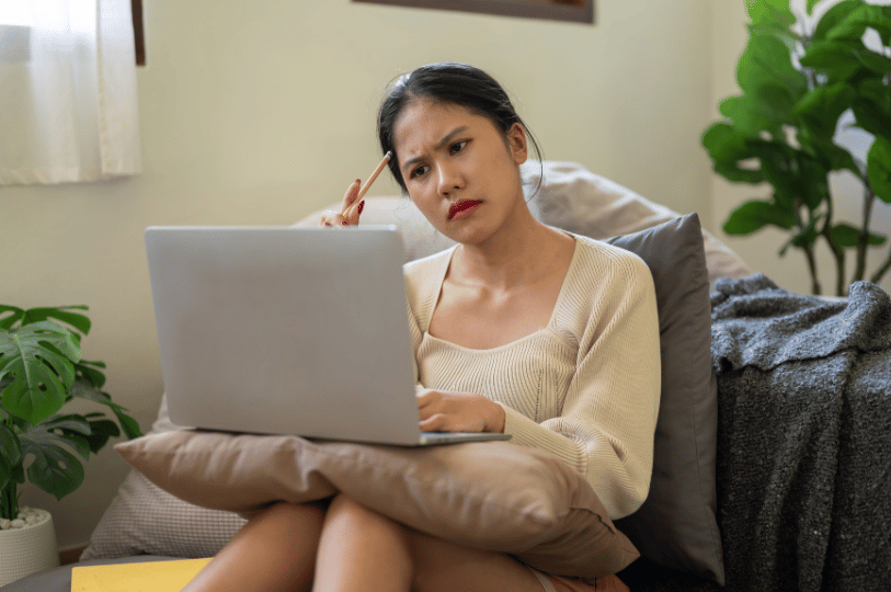 A frustrated woman holding a pencil and looking at her laptop, representing a business owner confused why their restaurant isn't showing on Google Maps.