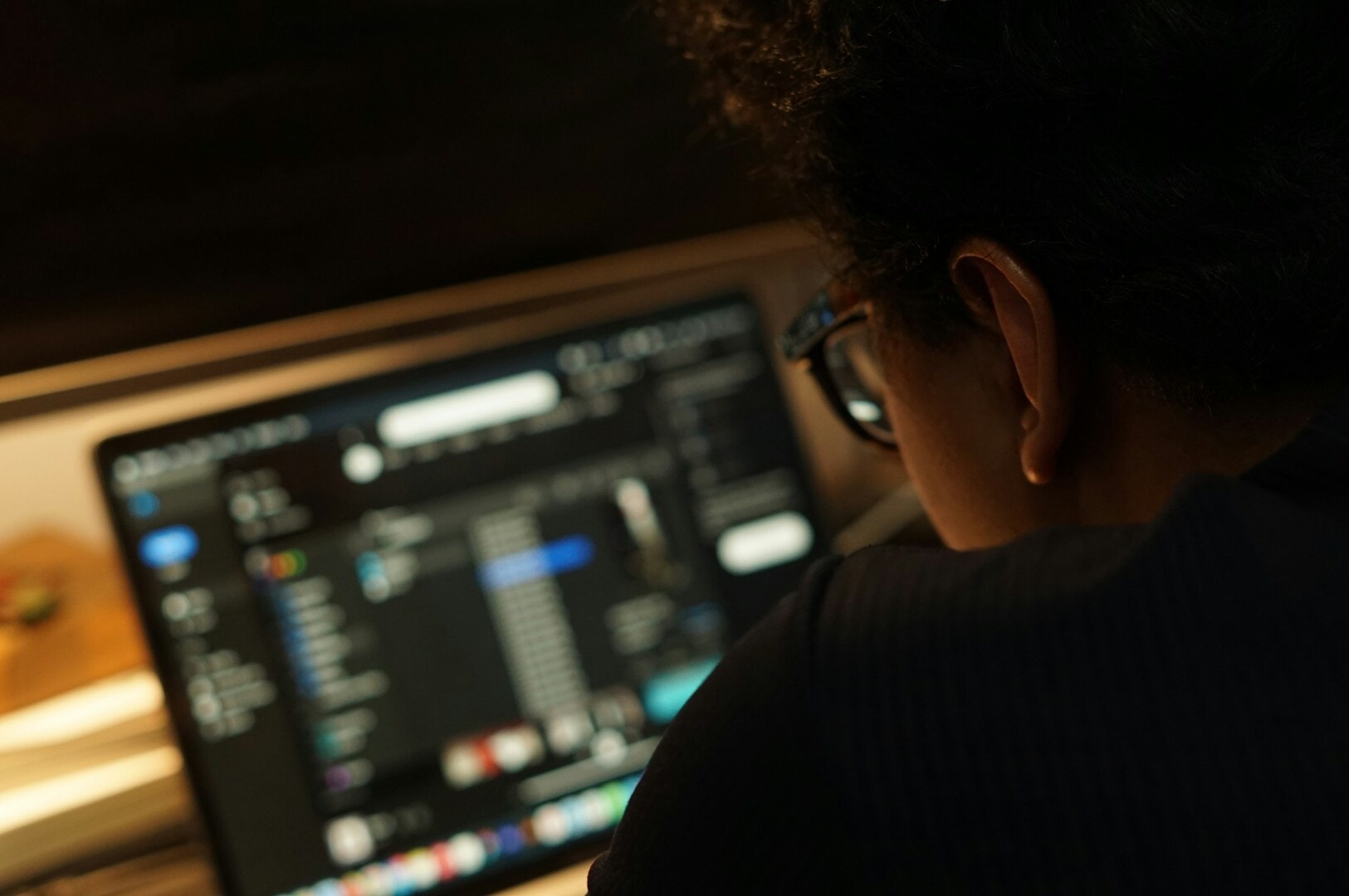 A person with glasses focuses intently on a blurred computer screen, suggesting concentration and a dimly lit, contemplative atmosphere.