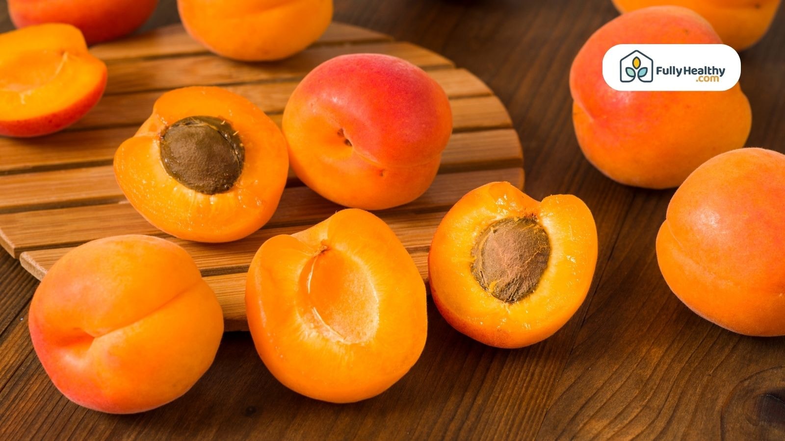 Sliced apricots showing seeds on a wooden board with whole apricots around them