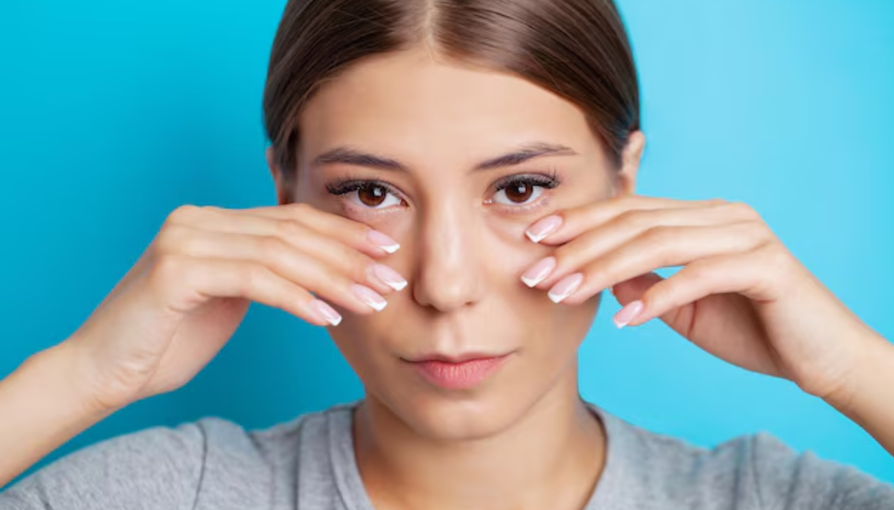Ung kvinne viser området under øynene med hendene foran ansiktet mot blå bakgrunn.