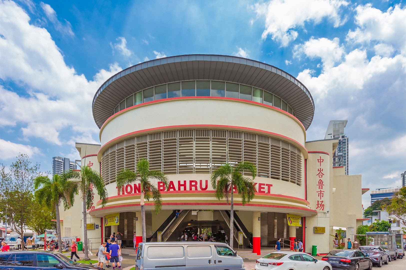 The circular, modernist exterior of the Tiong Bahru Market and Food Centre, with palm trees and a cloudy blue sky.
