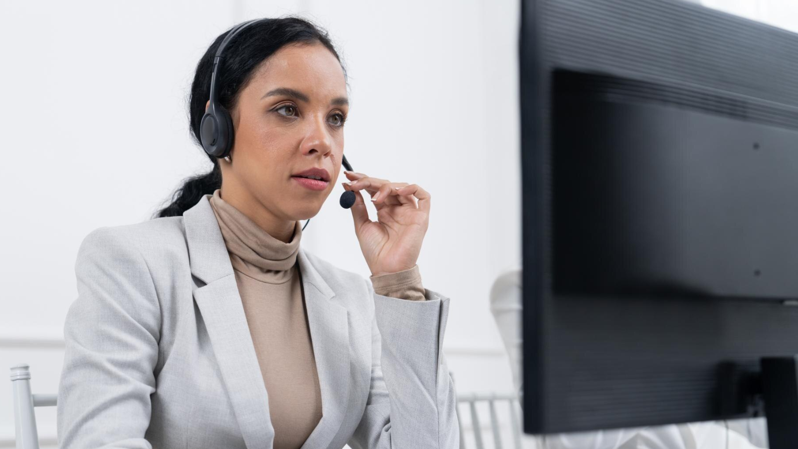 A businesswoman talks on a headset using call center voip while looking at a computer monitor