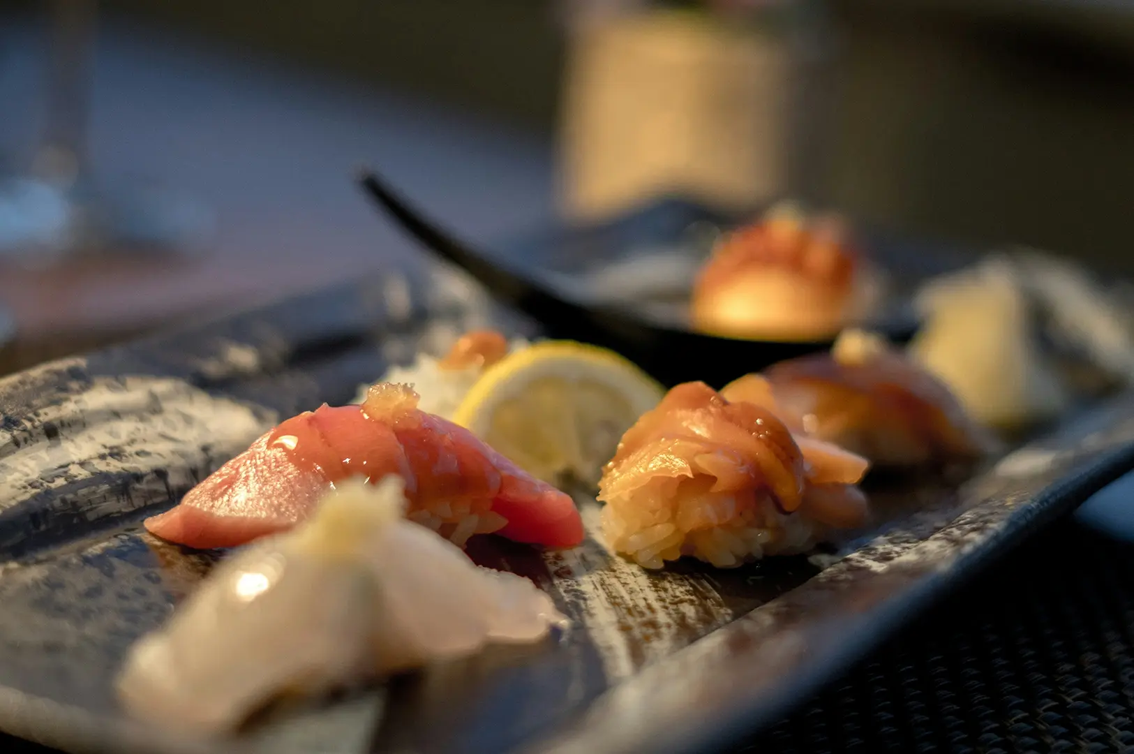 Close-up of various fresh nigiri sushi pieces arranged on a textured ceramic platter.