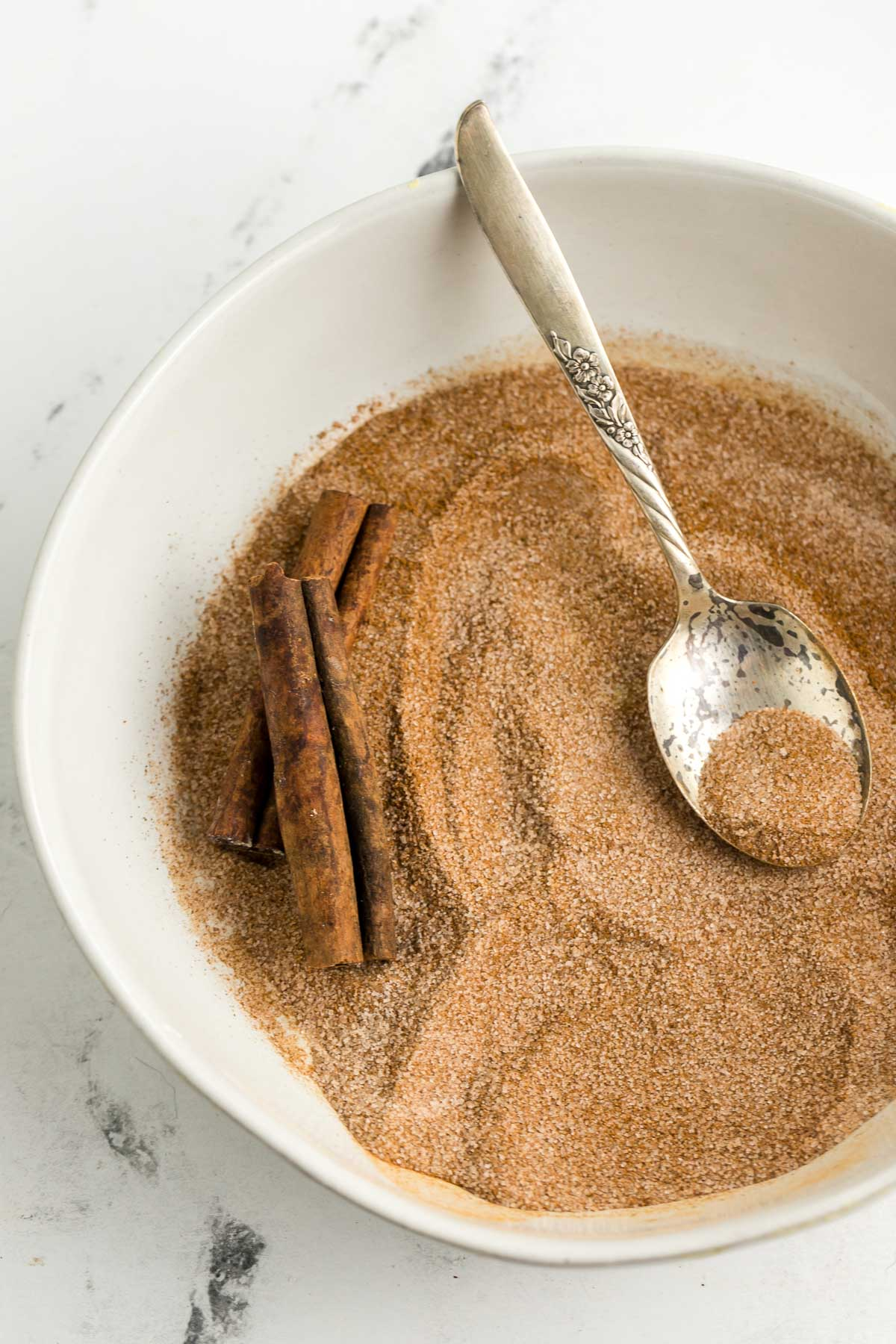 bowl of cinnamon sugar with cinnamon sticks and a spoon in it 