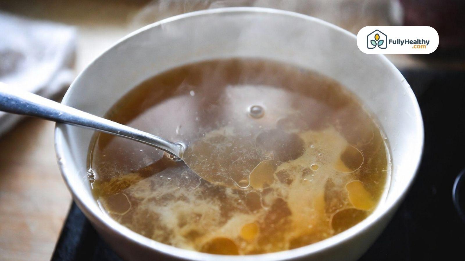 Close-up of broth in a bowl with visible oil droplets and spoon.