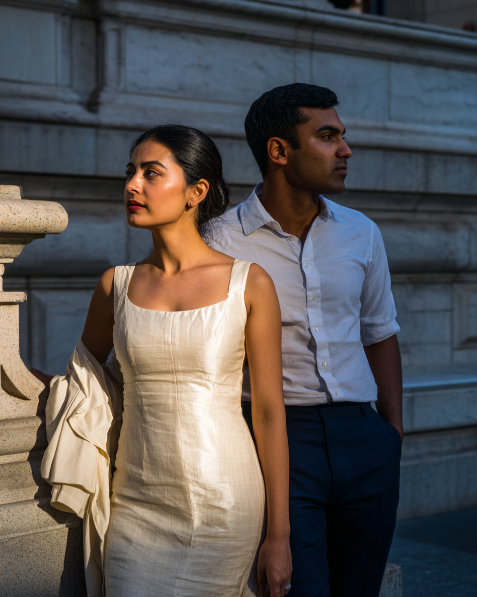 Attractive young heterosexual American couple of Indian descent on the steps of the New York Public Library in late afternoon light, representing the high-achieving professionals across NYC's diverse communities who pursue Gottman Method couples therapy at New York Therapy.
