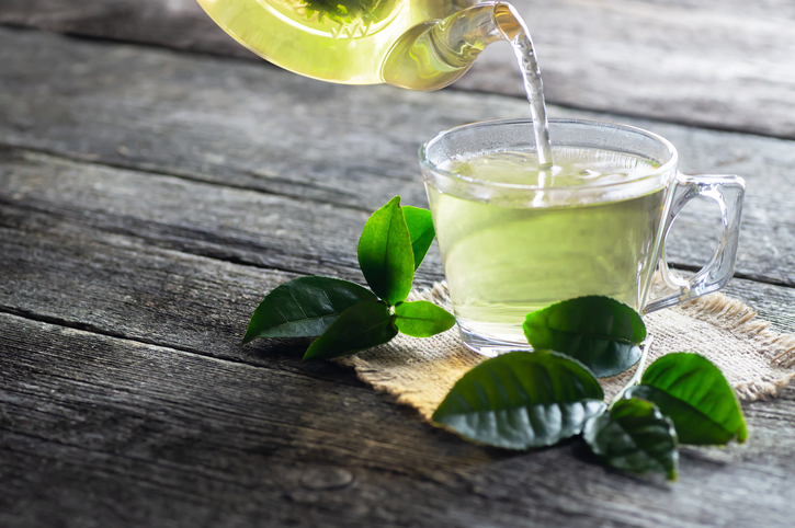 An image of a glass pitcher pouring green tea into a cup. 