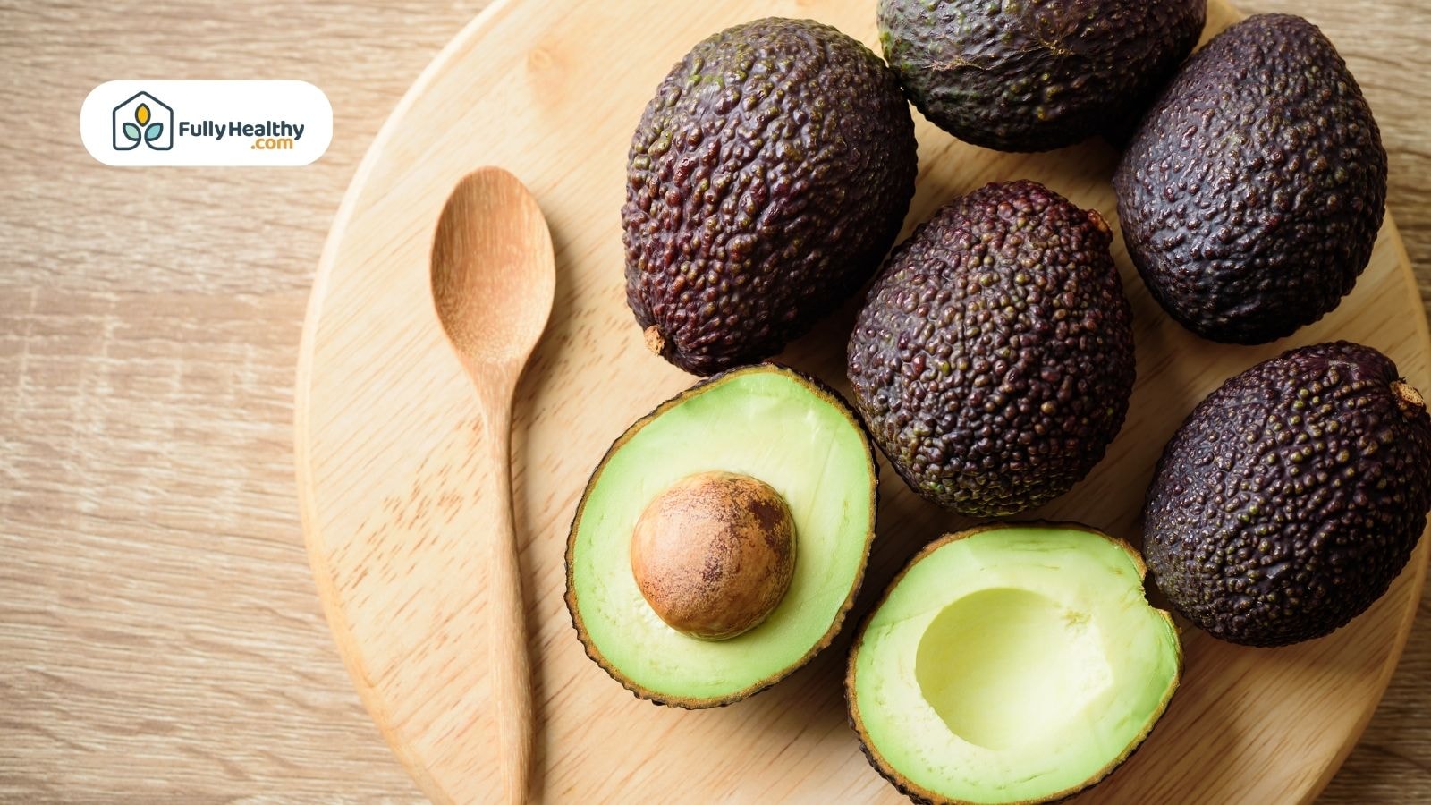 Whole and halved ripe Hass avocados on wooden plate