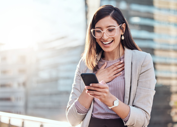 Smiling dark haired woman in pink glasses reading a message on her phone.  