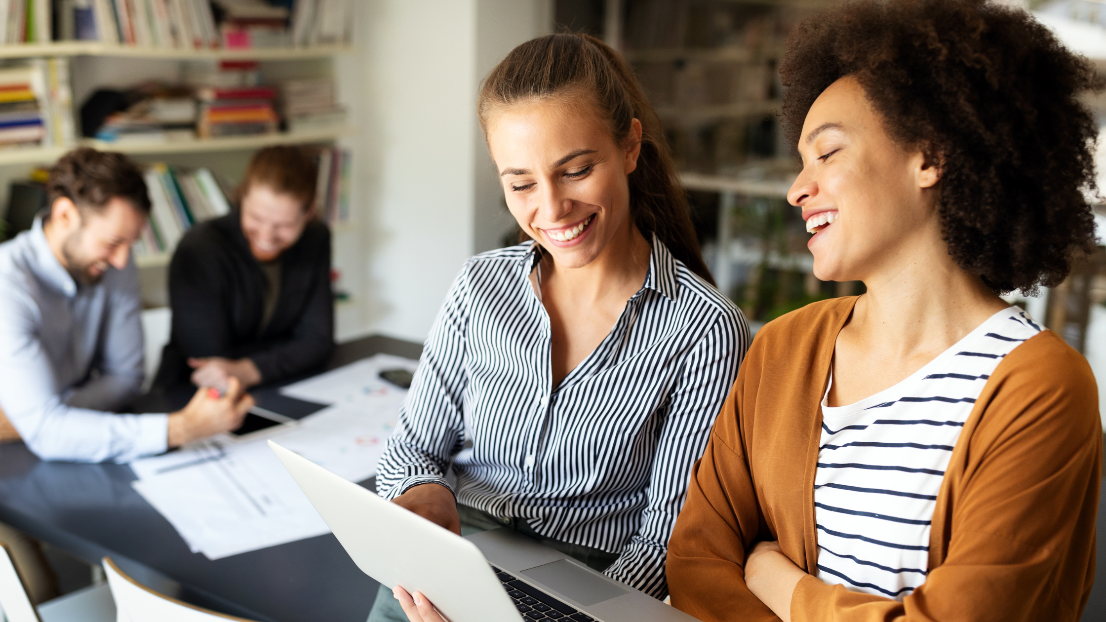 Two women smiling while viewing a laptop, representing teamwork in managing telecom expenses through seamless integration and comprehensive solutions.