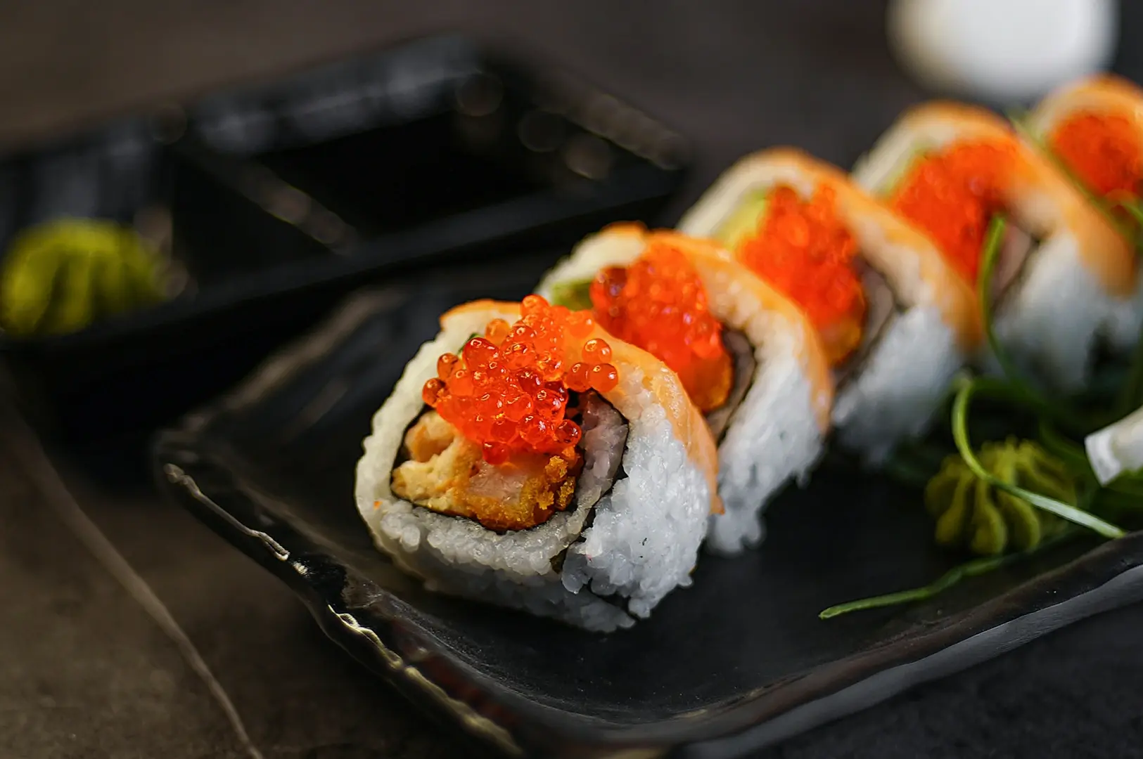 A row of maki sushi rolls filled with tempura and topped with salmon and bright orange fish roe.