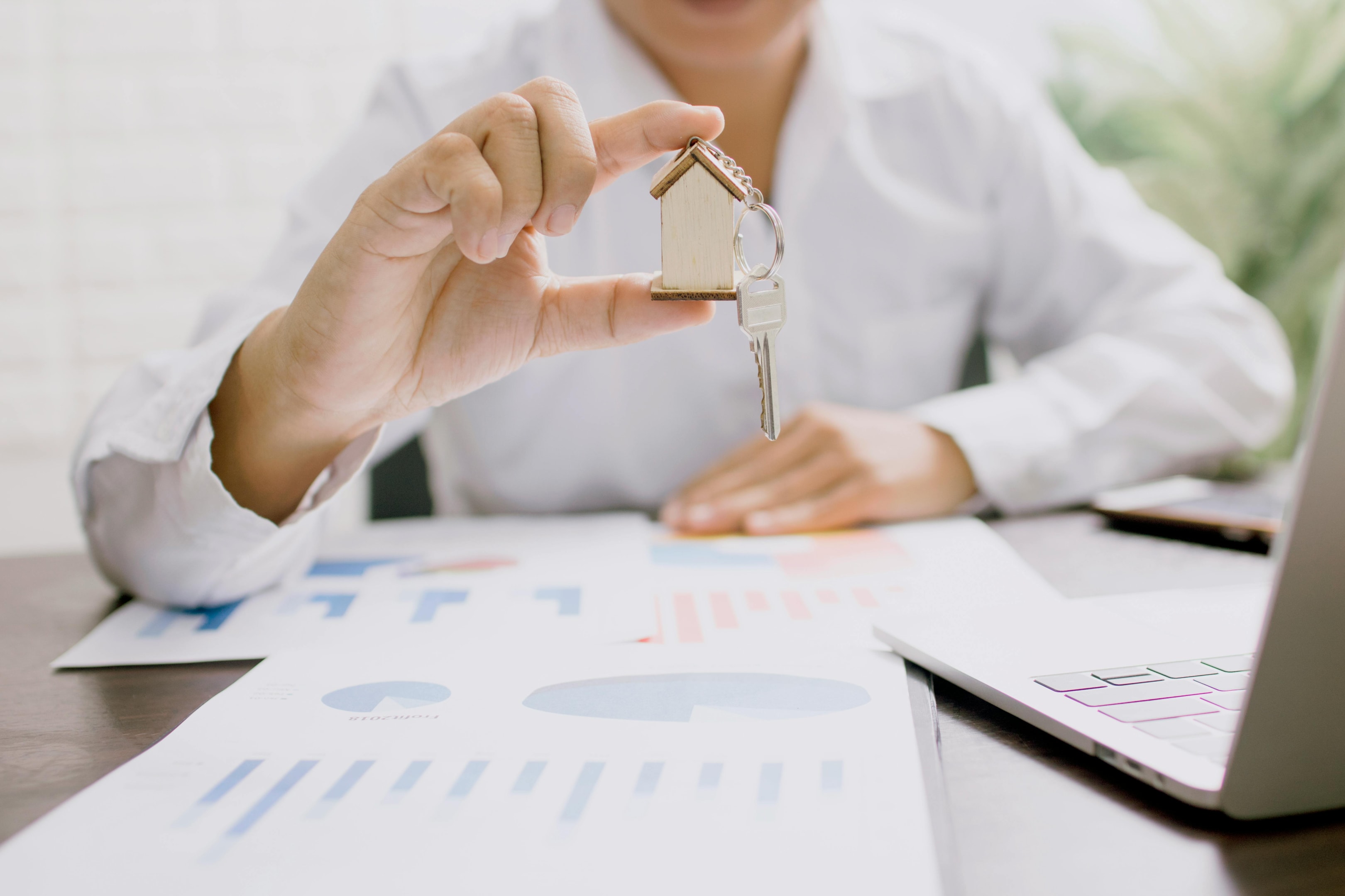 Real estate investor holds property keys with miniature model home keychain attached.