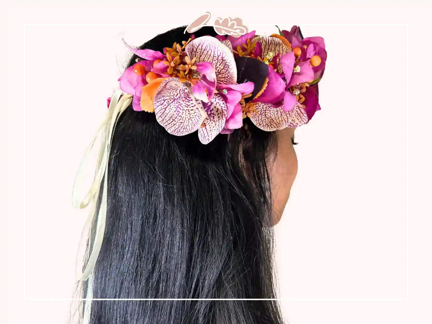 A woman with long black hair wearing a vibrant floral headpiece featuring pink and orange flowers. Tropical Elegance Floral Crown by Fabulous Flowers and Gifts.