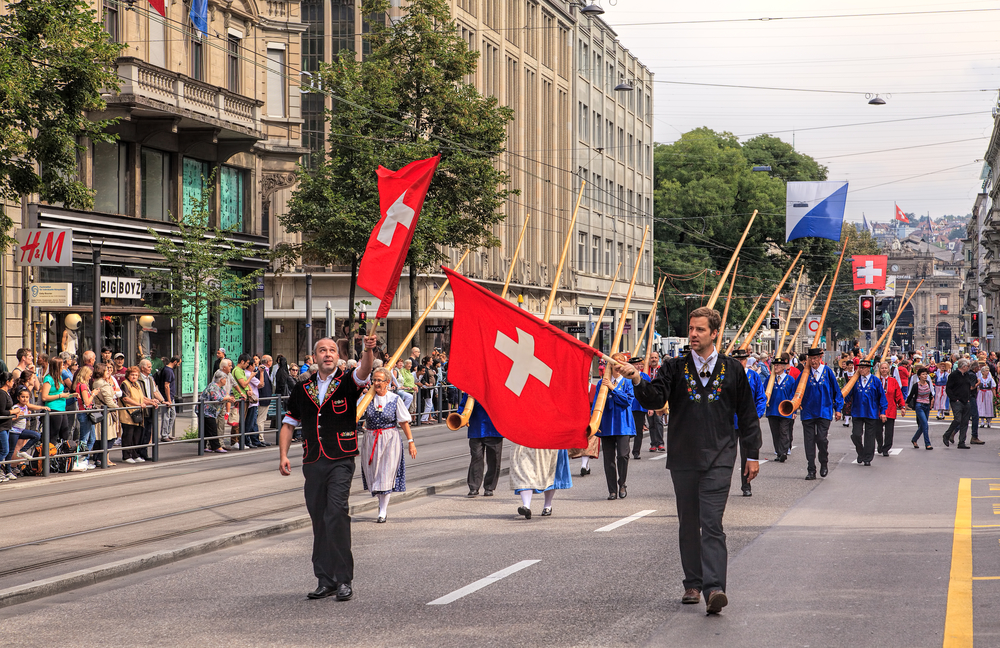 Tradtional parade in Zurich with Swiss flags, black slip on shoes and straw hats and gold lace caps.