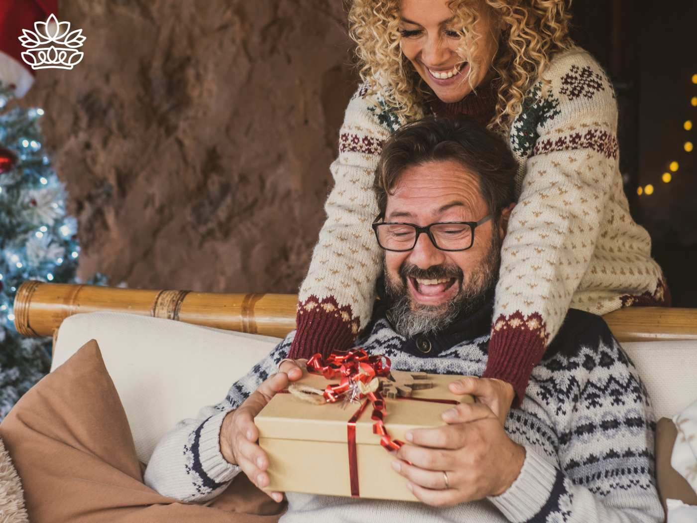 A cheerful man receiving a beautifully wrapped gift box from a woman, both in festive sweaters, representing the Gift Boxes for Him Collection - Amazing gift ideas wrapped in magic - Fabulous Flowers and Gifts