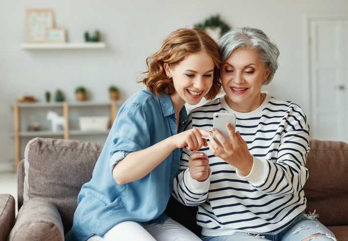 Granddaughter and grandmother smiling and pointing at something on a cell phone.  