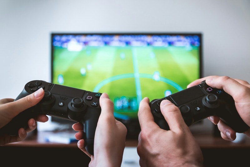 Two people hold video game controllers, playing a soccer game on a large TV screen.