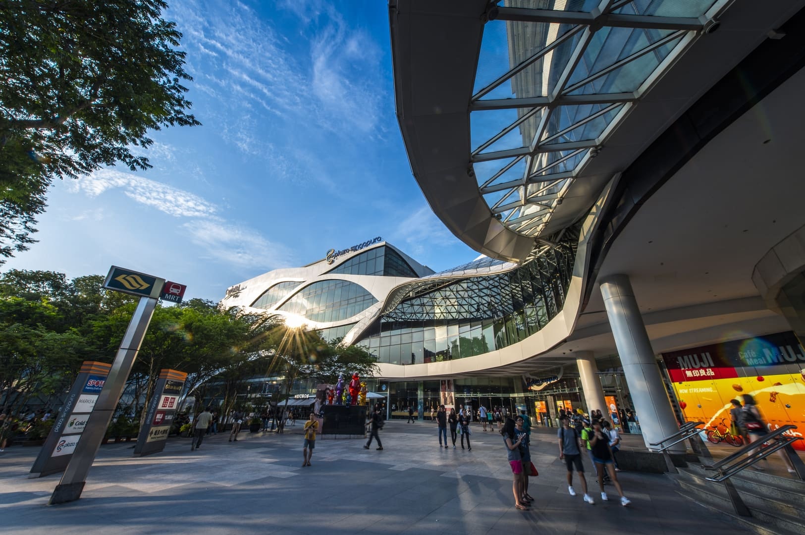 A large building with a curved roof, known as Plaza Singapura, set against a clear blue sky.