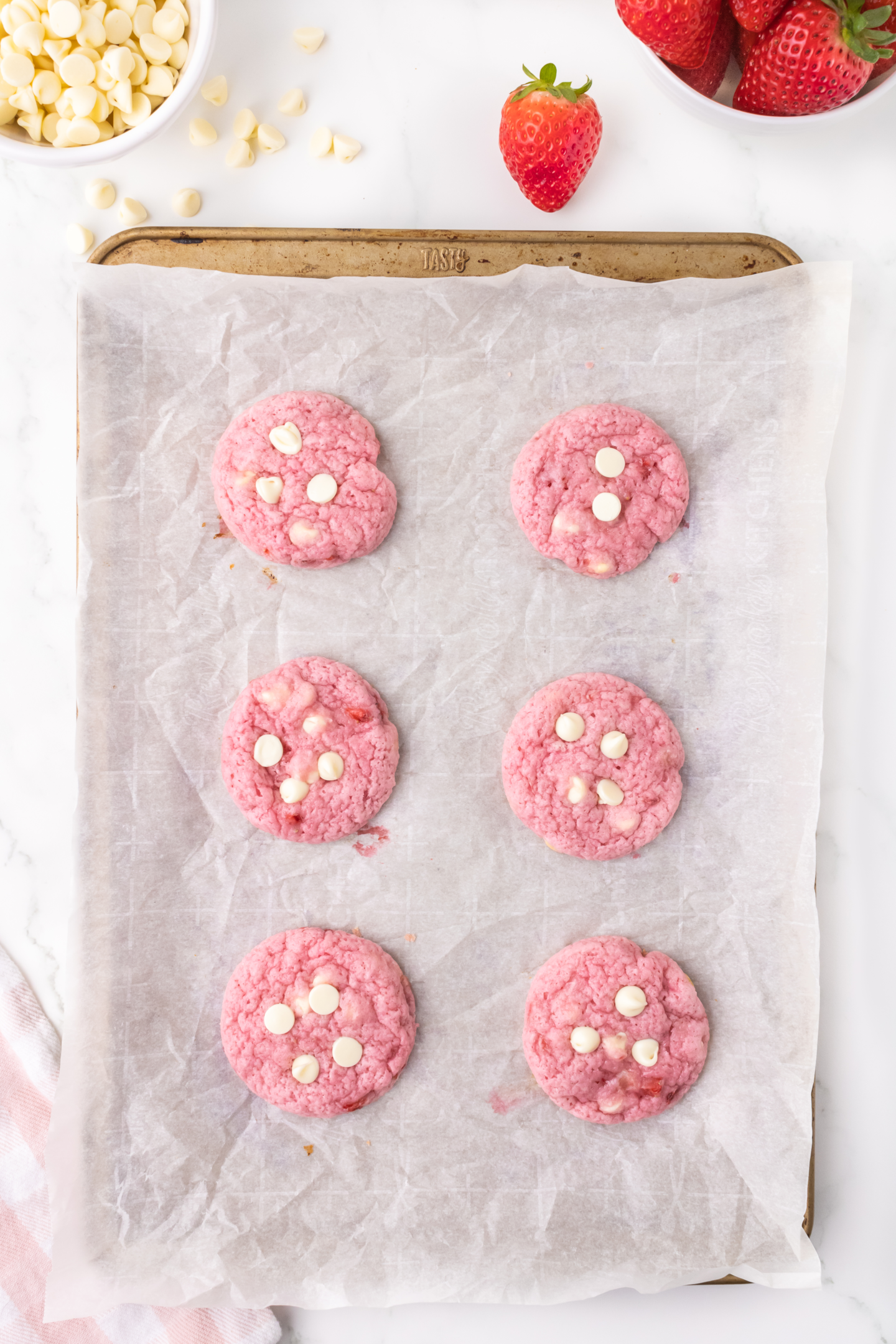 six baked strawberry white chocolate cookies topped with white chocolate chips on baking sheets with parchment paper