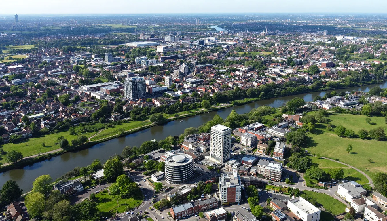 An aerial view of Reading showcases the River Thames winding through the town, with the bustling town centre buildings and surrounding residential neighborhoods interspersed with green spaces, highlighting its appeal as one of the best places to live in the UK. The scene captures the community's vibrant life, with easy access to excellent transport links, making it a fantastic place for families and young professionals alike.