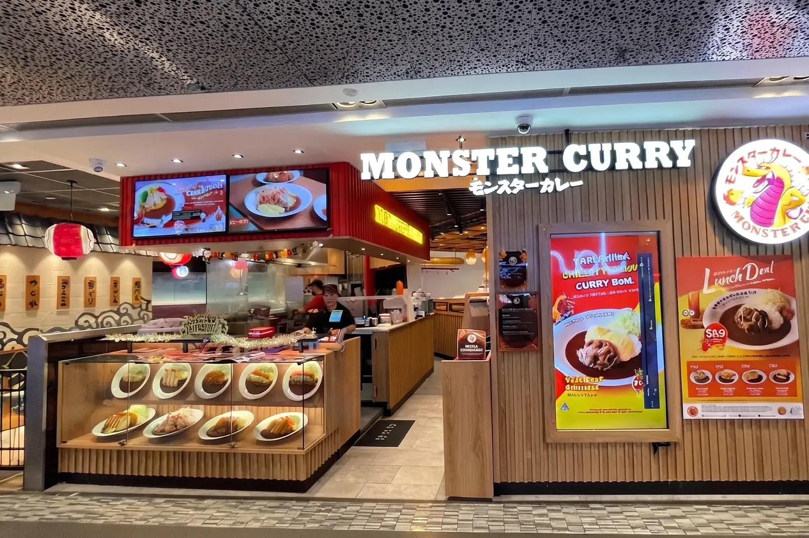 Storefront of Monster Curry Japanese restaurant featuring a display case of food samples and a lunch deal menu.