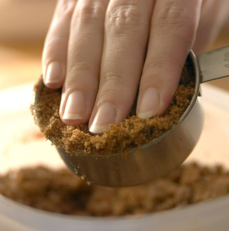 hand packing brown sugar into a cup