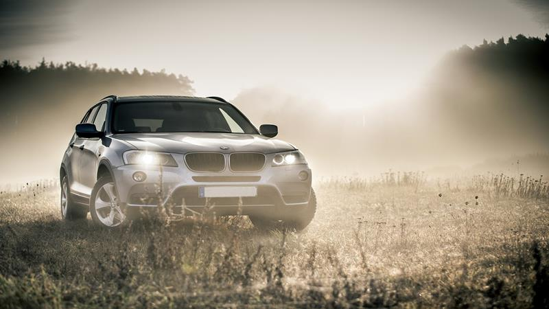 BMW SUV in a field with headlights on.