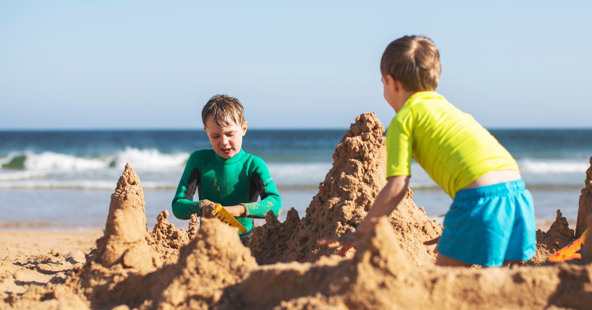 Children building sandcastles on the Ocean City NJ beach near Gardens Plaza, representing family fun on the South Jersey Shore.