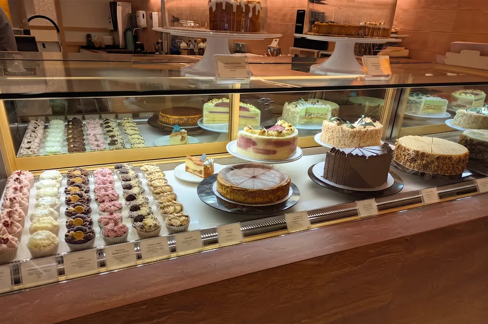 Glass pastry display counter showcasing whole cakes, cheesecakes, and rows of cupcakes.