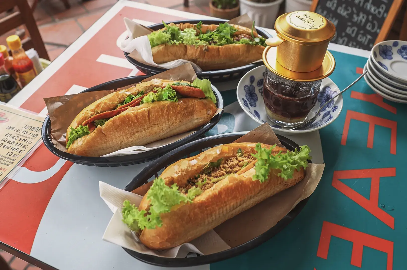 Vietnamese bánh mì sandwiches with fresh lettuce and savory fillings served alongside traditional drip coffee at a local café in Singapore.