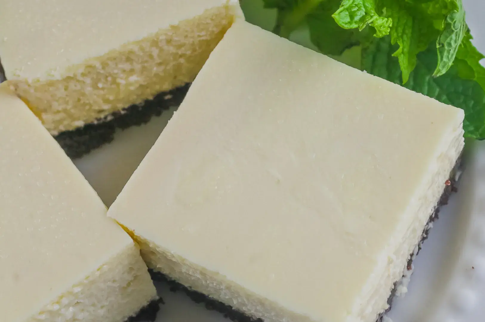 Three squares of creamy dessert on a plate, garnished with fresh mint leaves.
