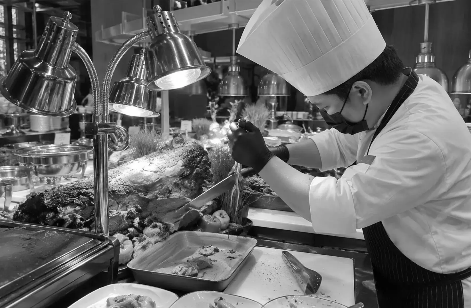 Chef carving roasted meat at a live buffet station with warm lighting and professional kitchen setup.