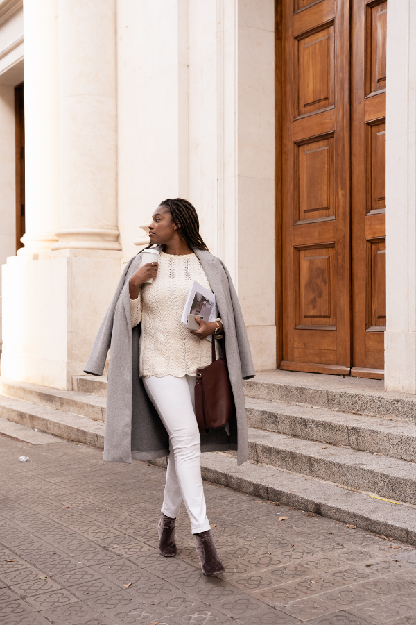 a woman carrying a magazine and bag walks along a street
