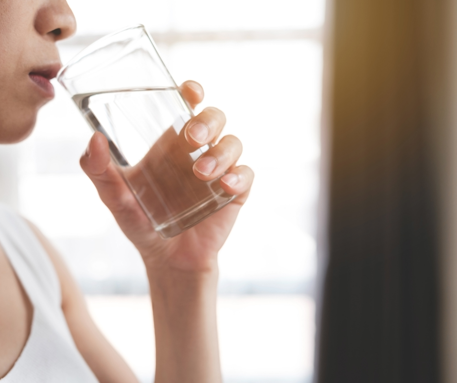 A person drinking a glass of water with a caption "Hydration and fluid intake can help manage constipation after quitting drinking"