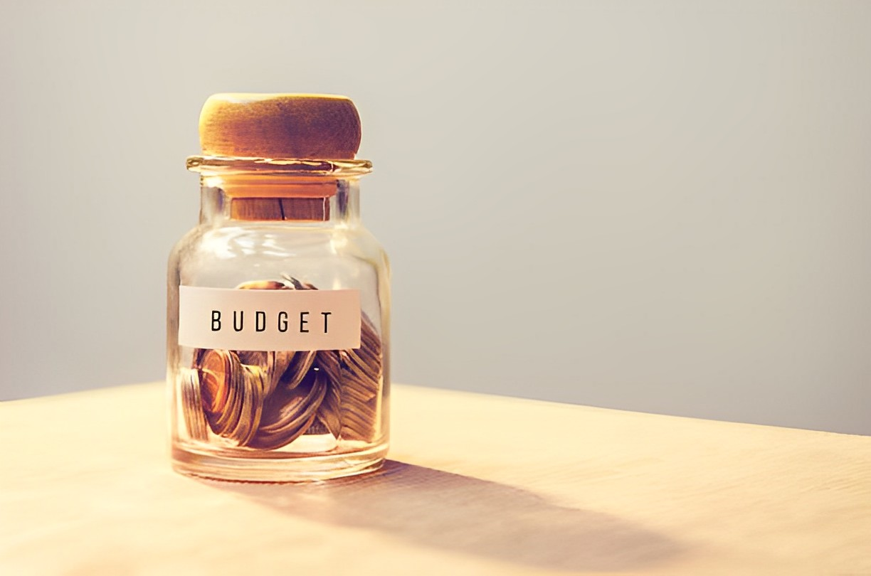 A photo of a jar with a budget sign and has coins inside of it