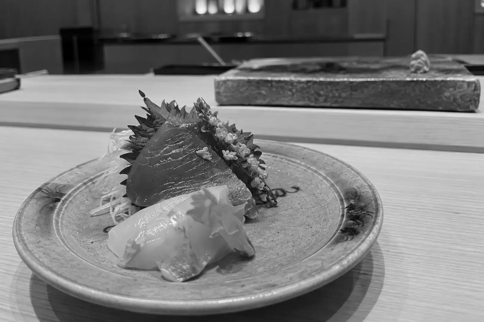 Individual sashimi serving arranged on a ceramic plate with shiso leaves, shredded daikon, flowers, and decorative garnishes.