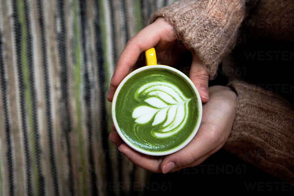 A person holding a cup of green coffee