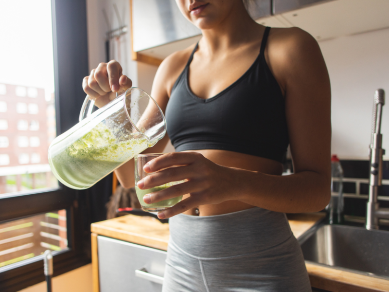 A woman pouring her green detox drink into a glass.