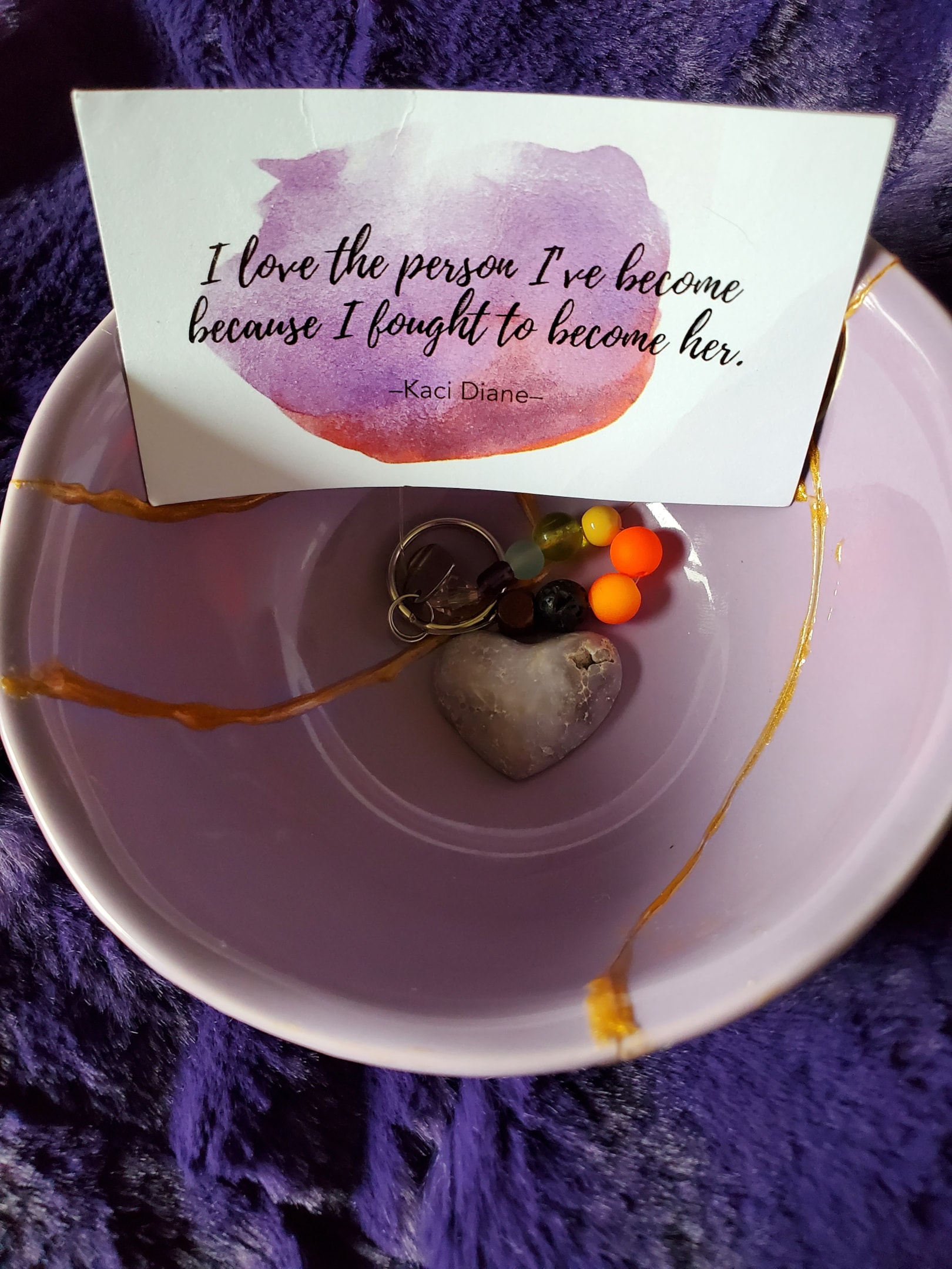 A photo of the inside of the author's Kintsugi bowl, with a quote on a card that reads, "I love the person I've become because I fought to become her" by Kaci Diane.