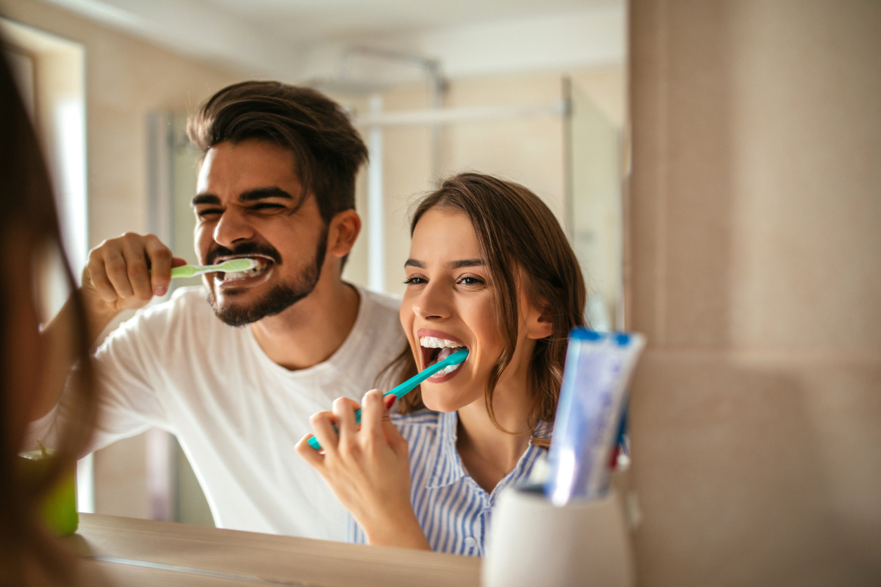 An image of a man and woman brushing their teeth in the bathroom mirror, showing the importance of oral care and throat health.