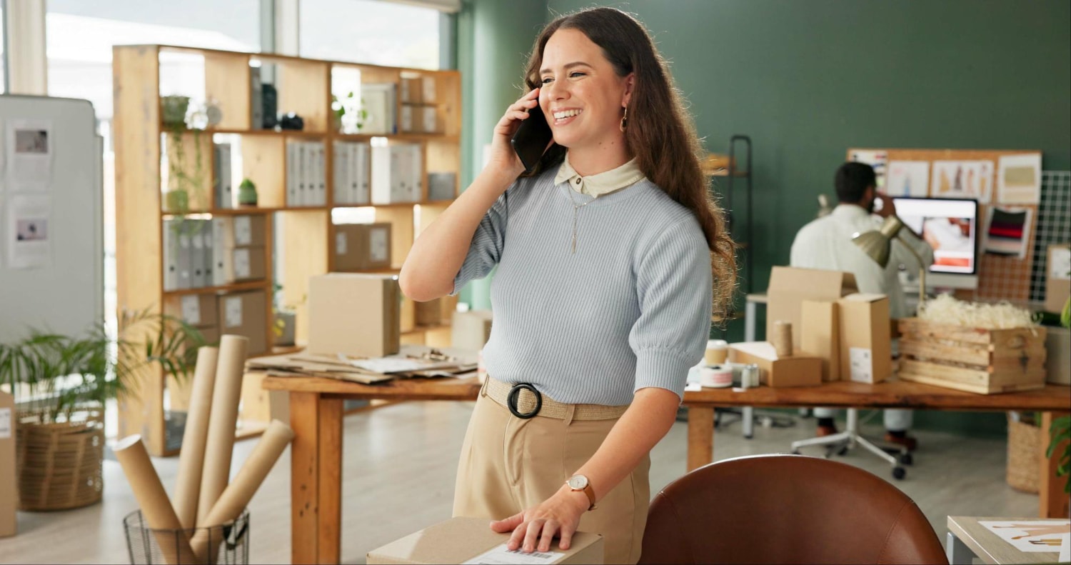 Entrepreneur in a product-focused workspace using a mobile device, showcasing how reliable VoIP services and unified communications enhance business operations in e-commerce and logistics.