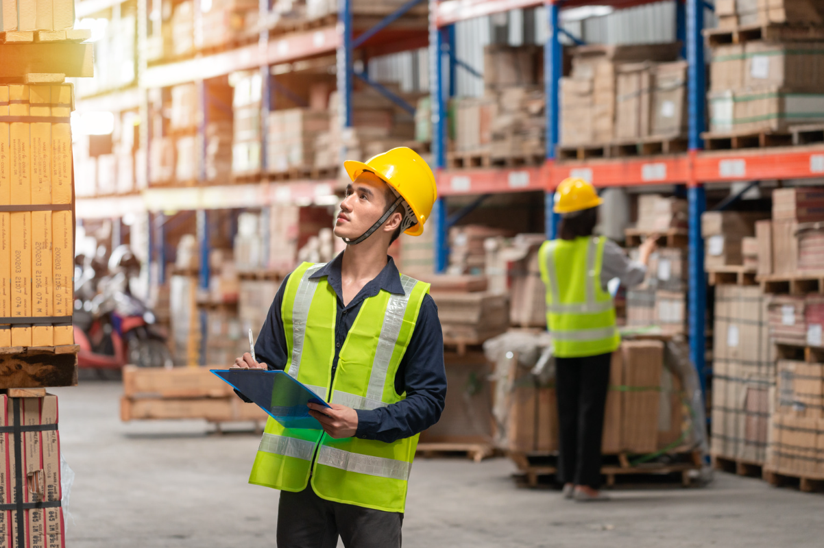 Warehouse inspector in hard hat and holding a clipboard inspecting storage.