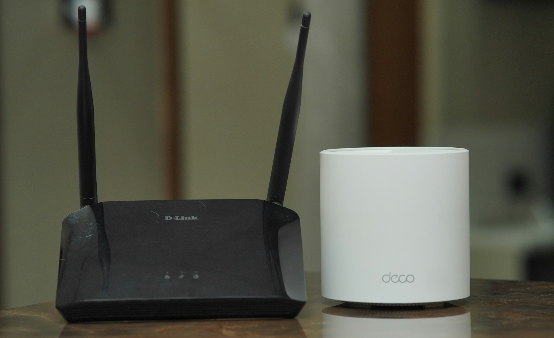 A black D-Link router with two anternnas flanked to the right by a white cylindrical Deco router